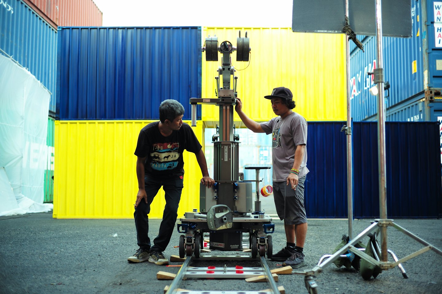 Two crew members assemble a camera dolly on industrial tracks.